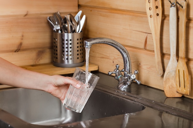 Faucet tap water pours water into glass in female hand