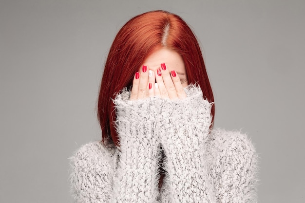 Fed haired unrecognizable woman wearing warm gray seater hiding face by hands