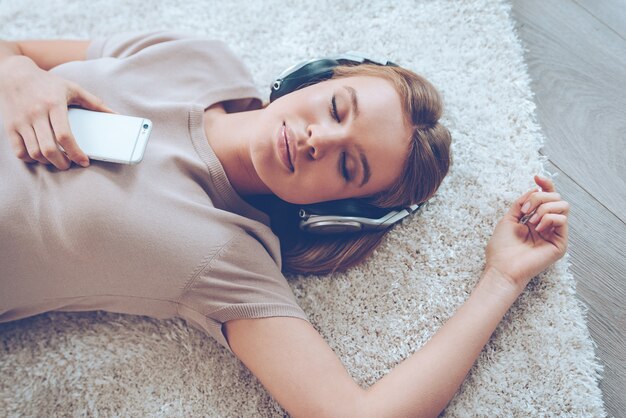 Photo feeling calm. top view of beautiful young woman listening to music and keeping eyes closed