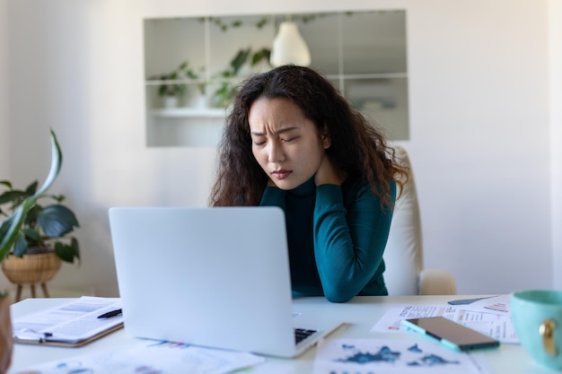 Feeling exhausted Frustrated Asian woman looking exhausted and massaging her neck while sitting at her working place