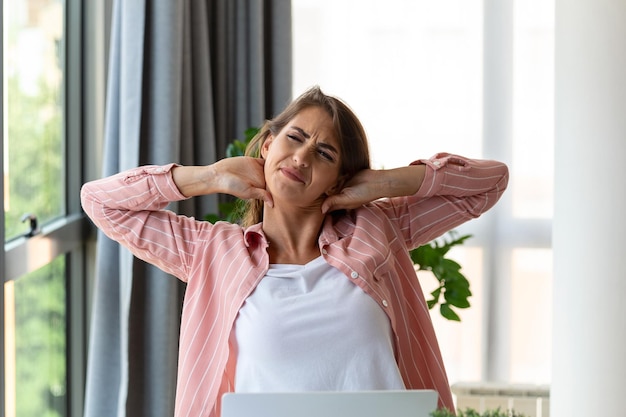 Feeling exhausted Frustrated woman looking exhausted and massaging her neck while sitting at her working place