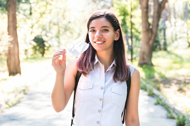 Feeling free. young woman alone in park removing medical mask and breathing cheerfully