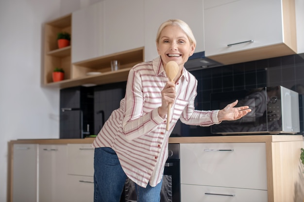 Feeling good. Blonde housewife having fun in the kitchen and smiling