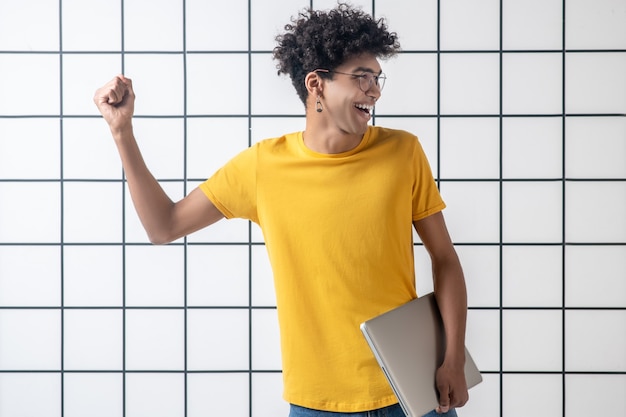 Feeling great. African american young guy in eyeglasses holding a laptop and feeling awesome