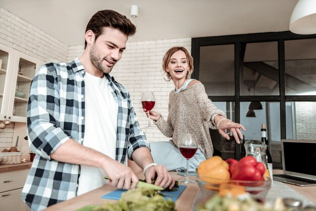 Feeling great. Dark-haired handsome man in a checkered shirt looking contented while cutting vegetables for breakfast