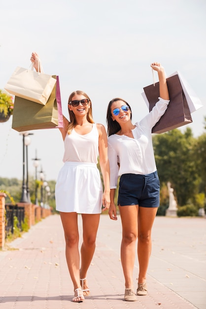 Feeling happy after day shopping. Full length of two beautiful young women showing their shopping bags and smiling while walking by the street together