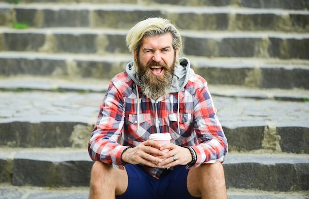 Feeling playful good morning inspiration brutal man with beard drinking tea from cup bearded man drink coffee outdoor hipster relax on stairs mature traveler having rest take away coffee