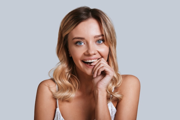 Feeling playful. Playful young woman looking at camera and smiling while standing against grey background