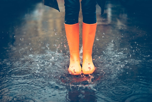 Feeling protected in her boots. Close-up of woman in orange rubber boots jumping on the puddle