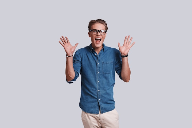 Feeling surprised.  Handsome young man gesturing and keeping mouth open while standing against grey background