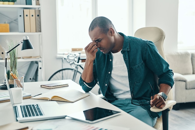 Feeling tired. Frustrated young African man in shirt massaging nose while sitting in the office