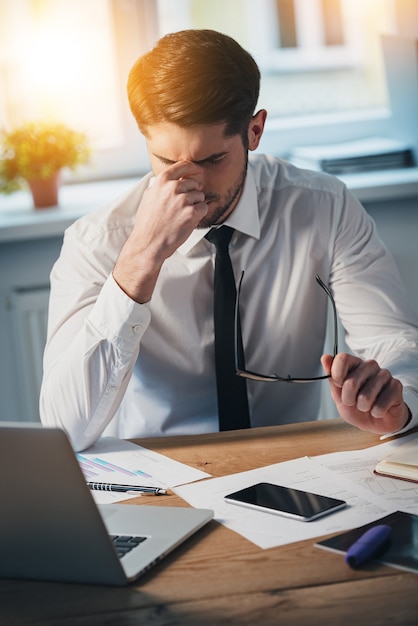 Feeling tired. Frustrated young handsome man looking exhausted while sitting at his working place