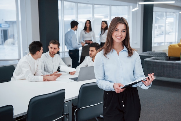 Feels good because she loves she's job. Portrait of young girl stands in the office with employees at background