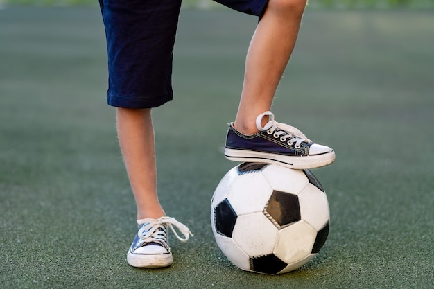 Feet of a child boy with a soccer ball on a green lawn on a football field