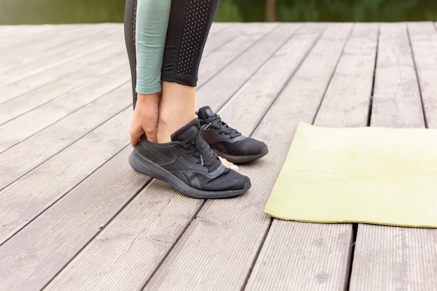 The feet of a girl taking off her black sneakers in front of a green sports mat