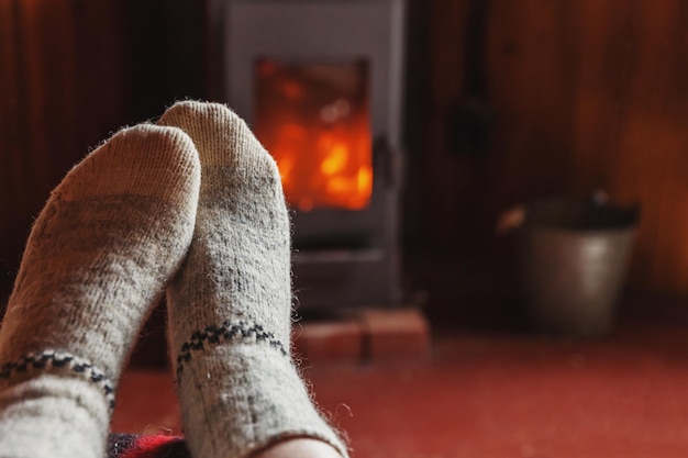 Feet legs in winter clothes wool socks at fireplace background woman sitting at home on winter or au