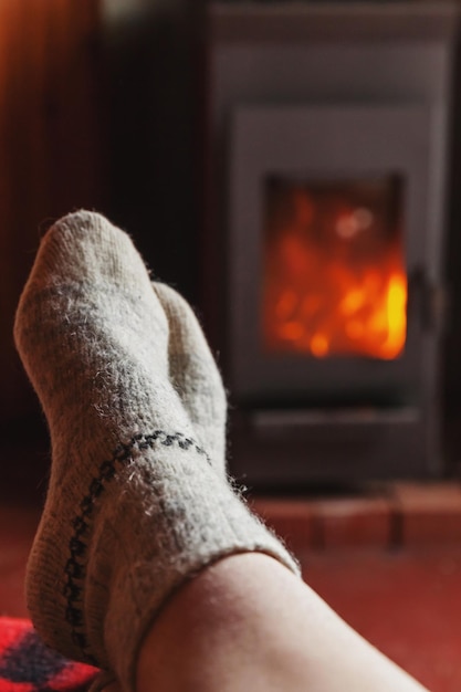 Feet legs in winter clothes wool socks at fireplace background woman sitting at home on winter or au...