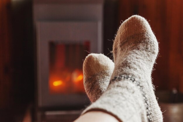 Feet legs in winter clothes wool socks at fireplace background woman sitting at home on winter or au...