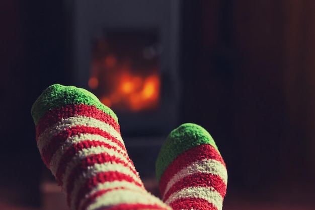 Feet legs in winter clothes wool socks at fireplace background Woman sitting at home on winter or autumn evening relaxing and warming up Winter and cold weather concept Hygge Christmas eve