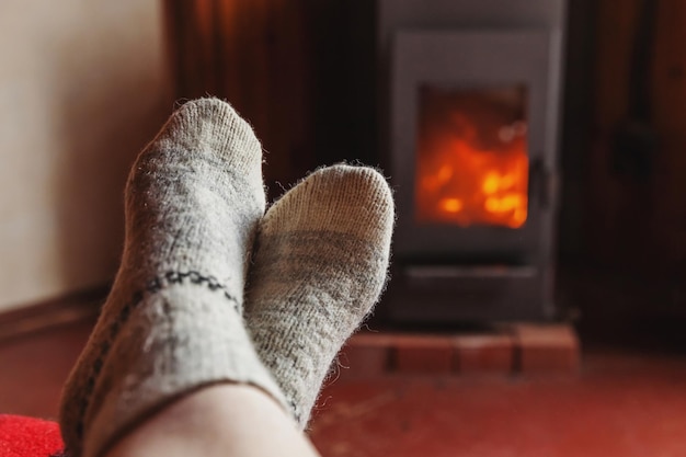 Feet legs in winter clothes wool socks at fireplace background Woman sitting at home on winter or autumn evening relaxing and warming up Winter and cold weather concept Hygge Christmas eve