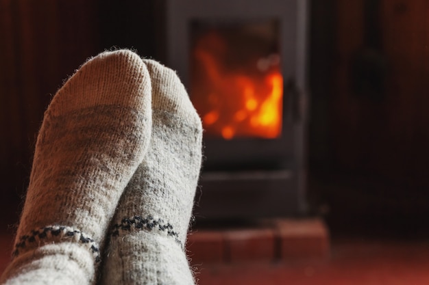 Feet legs in winter clothes wool socks at fireplace at home on winter or autumn evening relaxing and warming up