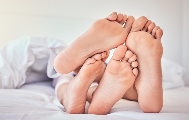 Feet love and a couple in bed to relax in the morning while bonding in their home for trust or support Bedroom sleeping or dreaming with a man and woman resting closeup under a blanket in a house