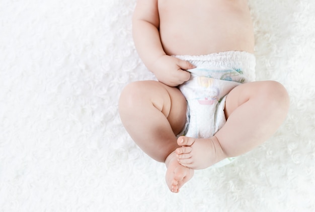 Feet of a six months old baby wearing diapers lying on the bed