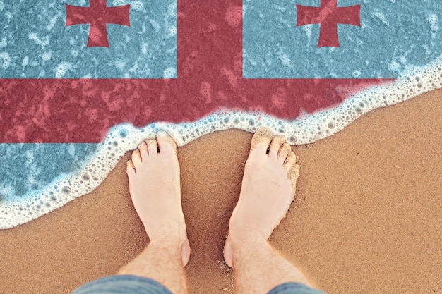 Feet on the sunny sandy beach with flag Georgia Top View on sea surf