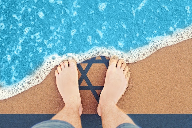 Feet on the sunny sandy beach with flag Israel Top View on surf