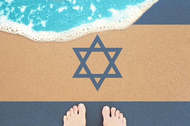 Feet on the sunny sandy beach with flag Israel View from top on surf