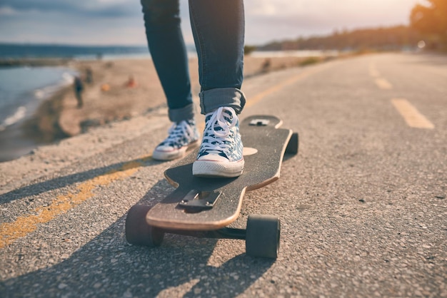 Feet of woman in sneakers on a longboard at the evening