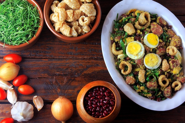 Feijao Tropeiro typical dish of Brazilian cuisine, made with beans, bacon, sausage, collard greens, eggs, on rustic wooden table.