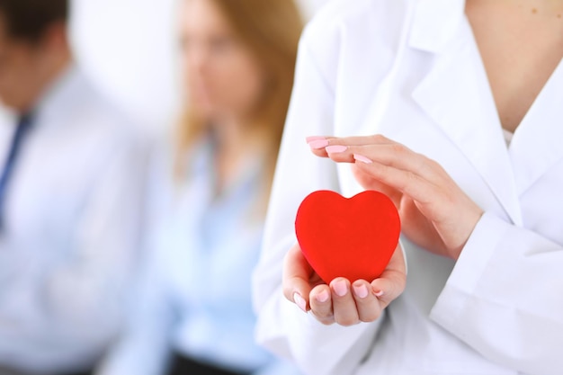 Femail doctor holding a red heart in his hands on a background of the patient. Health care concept