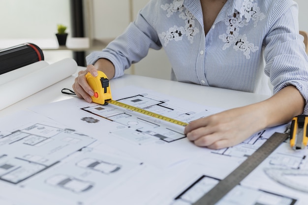 Female architect is using a tape measure to measure the house plans, She is checking the house plans that she has designed before sending them to the customers, She designs the house and the interior.