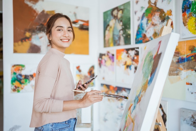 Female artist painting hold phone while working