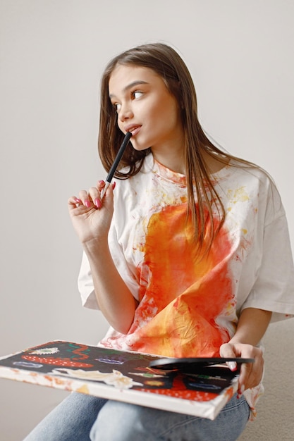 Female artist sitting on a chair near white wall holding a canvas and brushes