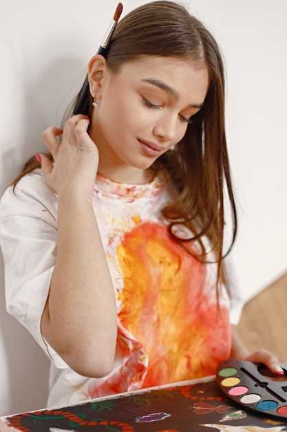 Female artist sitting on a chair near white wall holding a canvas and brushes