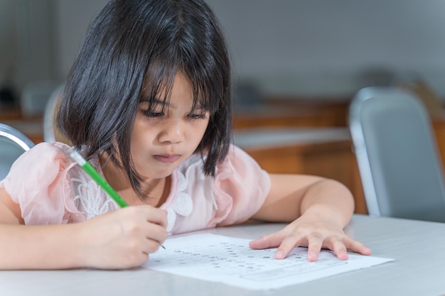 A female Asian kid student concentrate writing on the examination paper in the class