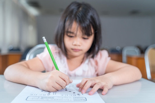 A female Asian kid student concentrate writing on the examination paper in the class