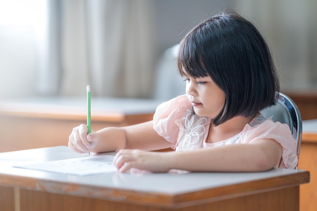 A female Asian kid student concentrate writing on the examination paper in the class