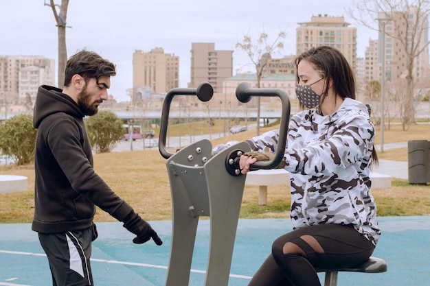 Female athlete using exercise equipment at park and her trainer showing how to do it