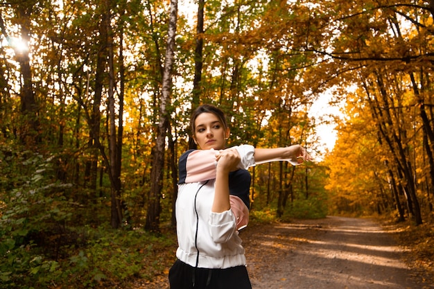 Female athlete warming up before hard workout. Healthy lifestyle. Fitness sporty woman stretching before run early in the morning in forest area. Sunshine on background.