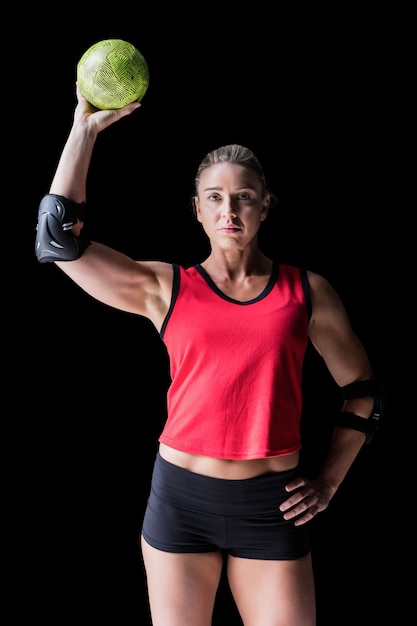 Female athlete with elbow pad holding handball on black