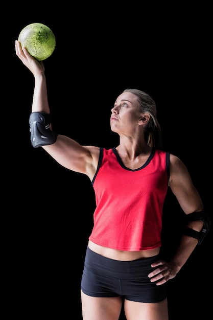 Female athlete with elbow pad holding handball on black