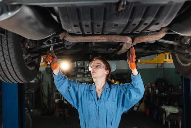 Female auto mechanic working under a car in a garage Portrait of a concentrated female mechanic the girl makes an inspection of the raised car writes down the damage on a sheet of paper