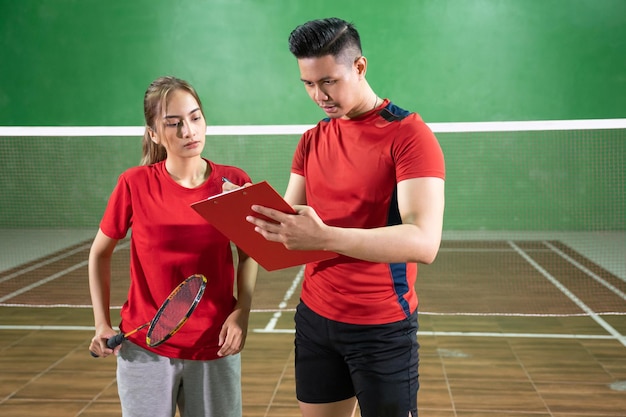 Female badminton player paying attention to coachs instructions with clipboard