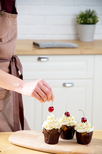 Female baker decorating cupcake with cherry and creme