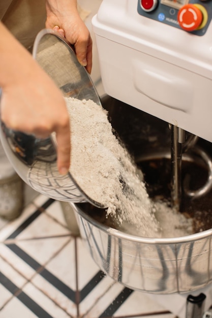 Female baker pouring flour in kneading machine at bakery