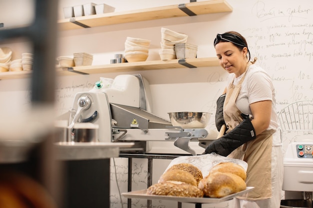 Female baker using a peel to take out a loaf of bread of the oven in a bakery