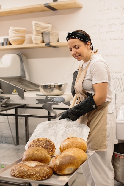 Female baker using a peel to take out a loaf of bread of the oven in a bakery